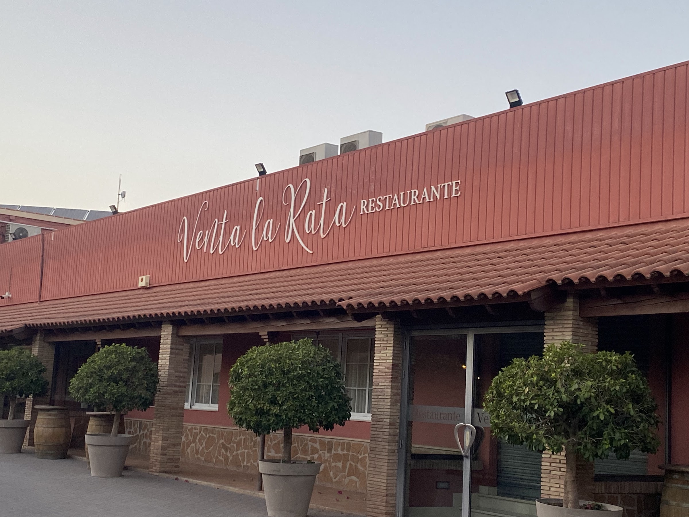 Fachada del Restaurante Venta la Rata al atardecer, con el rótulo manuscrito sobre el panel color terracota